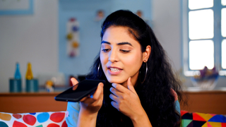 Lovely working Indian woman talking to her clients using the speaker of her smartphone