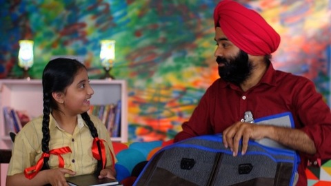A handsome Sikh Indian guy happily packing his daughter's bag pack for her school - parent-child bonding
