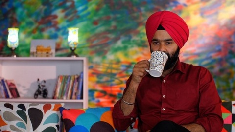 An Indian Sikh guy drinking tea / coffee while sitting alone on a comfortable sofa - beverage, morning breakfast